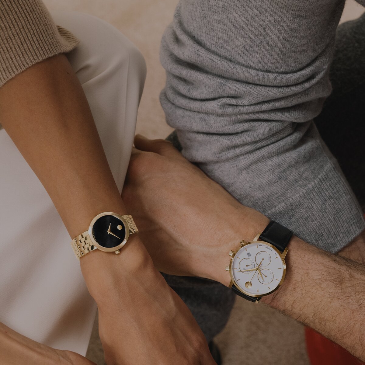 Woman wearing a gold tone Museum Classic bracelet watch with a black dial sitting next to a man wearing a Museum Classic Chronograph strap watch with white chronograph dial.
