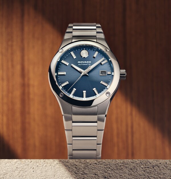 Museum Imperiale watch with silver bracelet and blue dial sitting on a stone ledge in front of a wooden wall.