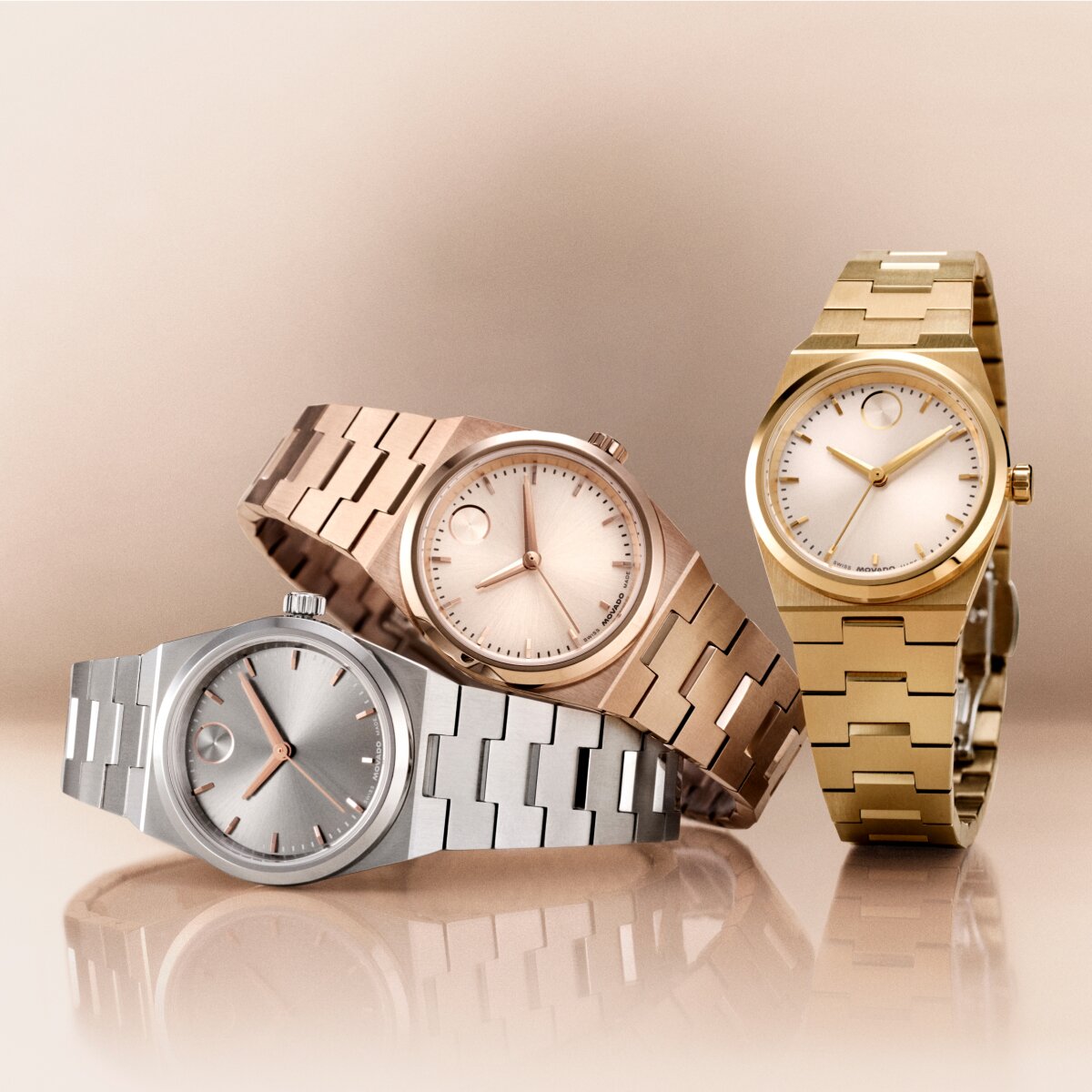 Stainless steel BOLD Quest Mini watch laying underneath a Rose gold tone BOLD Quest Mini watch with a Gold tone BOLD Quest Mini watch upright next to them.