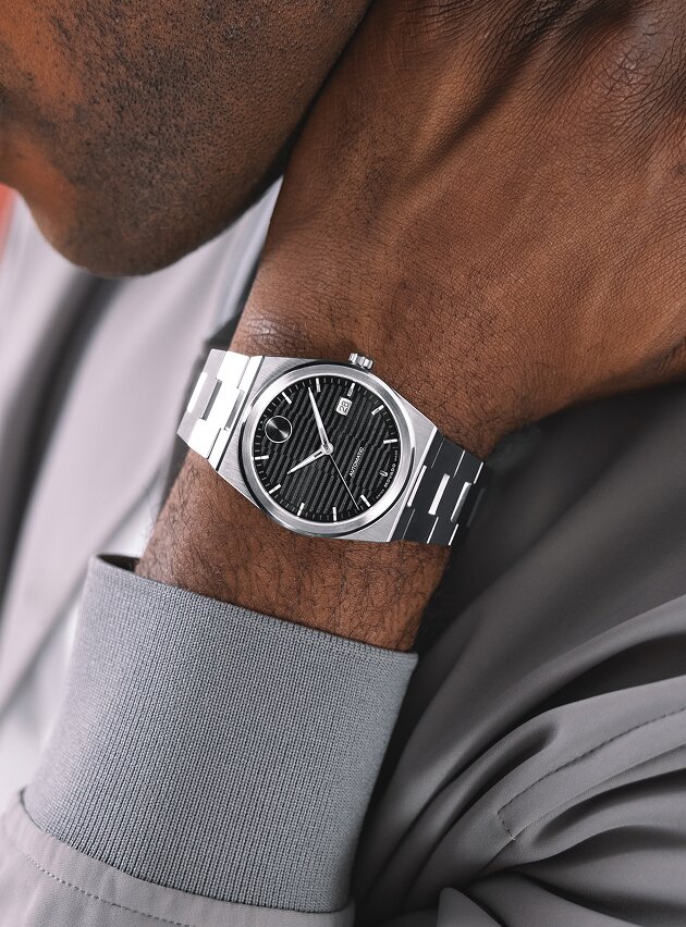 Man in a grey jacket wearing the BOLD Quest automatic watch with stainless steel bracelet and black dial.