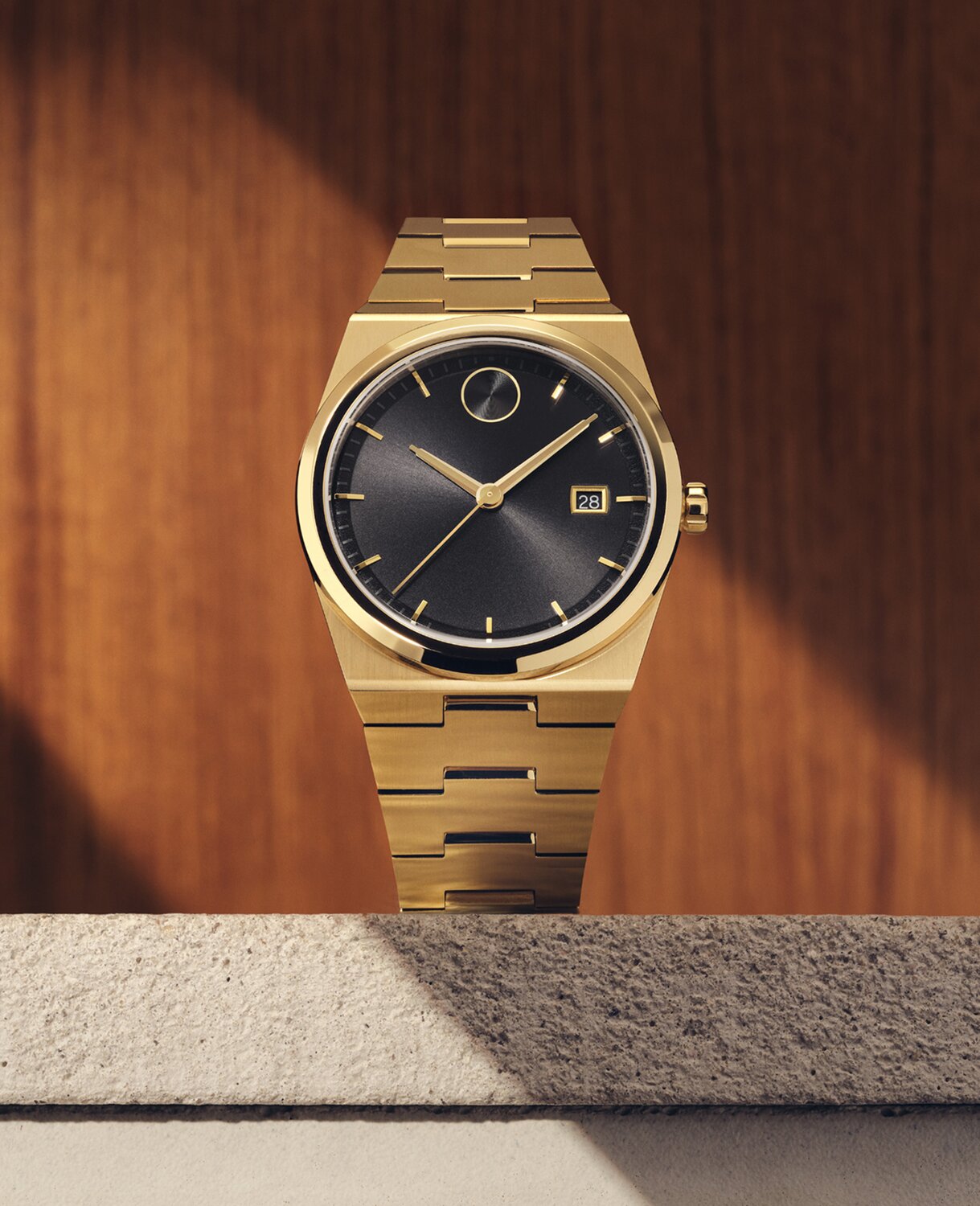 BOLD Quest watch with gold tone bracelet and black dial sitting on stone in front of a wooden panel.