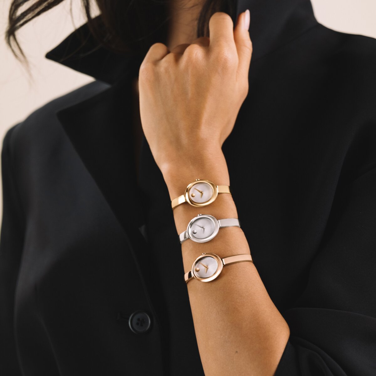 Woman in a black shirt wearing 3 Museum Bangle watches with an oval dial stacked on her wrist. Starting with the gold tone watch, followed by the silver watch and ending with the rose gold tone watch. 