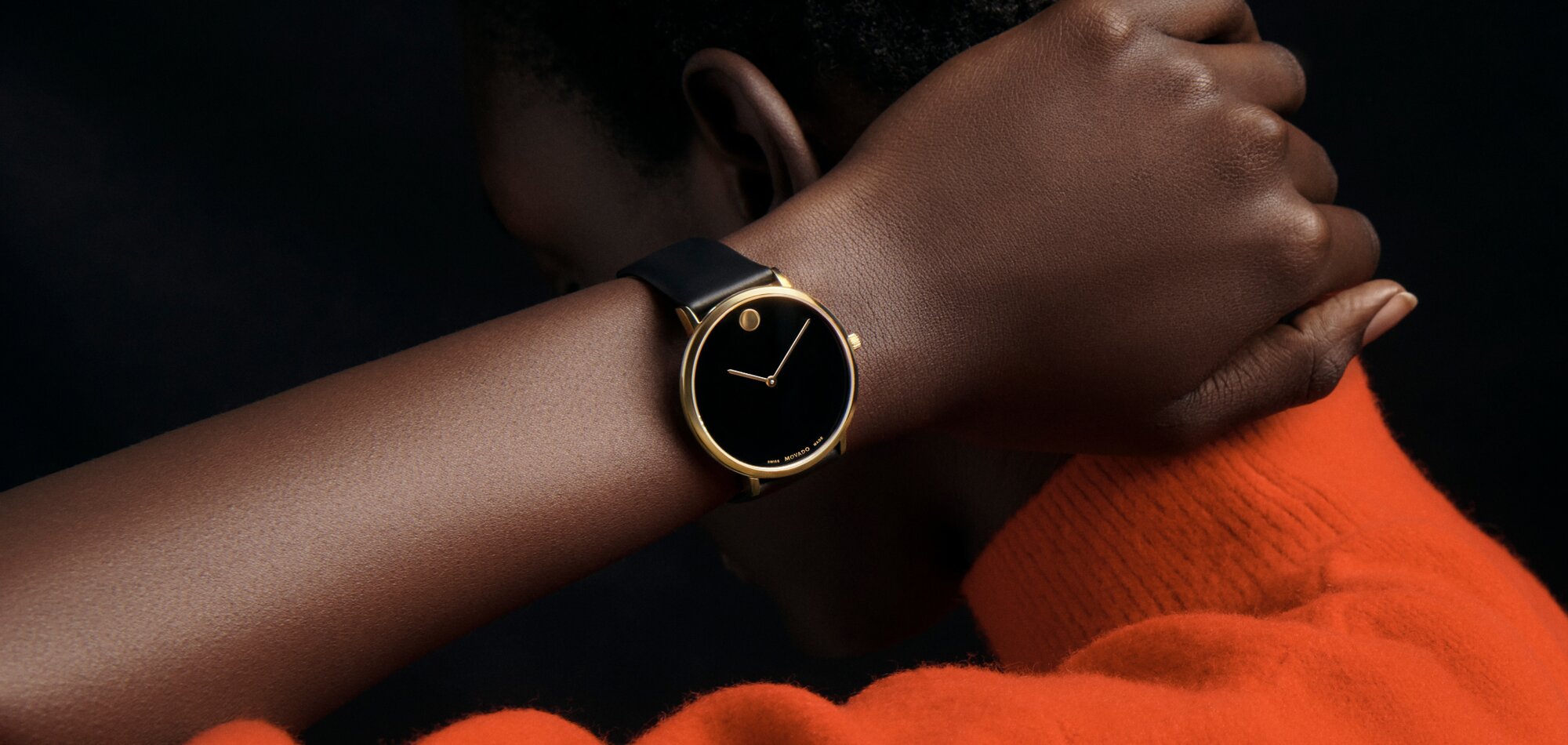 Woman in an orange seater wearing a Modern 47 watch with black strap, black dial and gold accents.