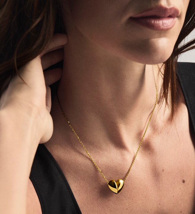Woman wearing a gold tone heart necklace.