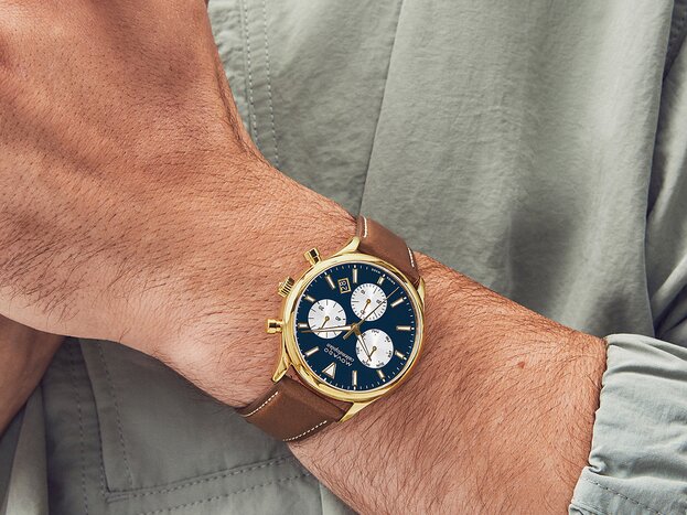 Man in a green jacket wearing the Heritage Calendoplan watch with brown strap and blue chronograph dial.