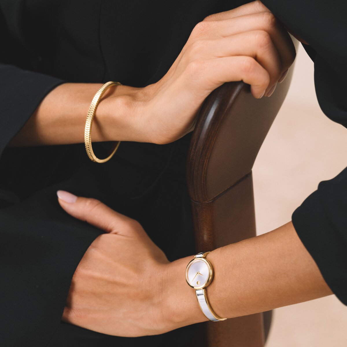 Woman in a black shirt and black pants wearing a gold bracelet and the silver Moda bangle watch with gold accents