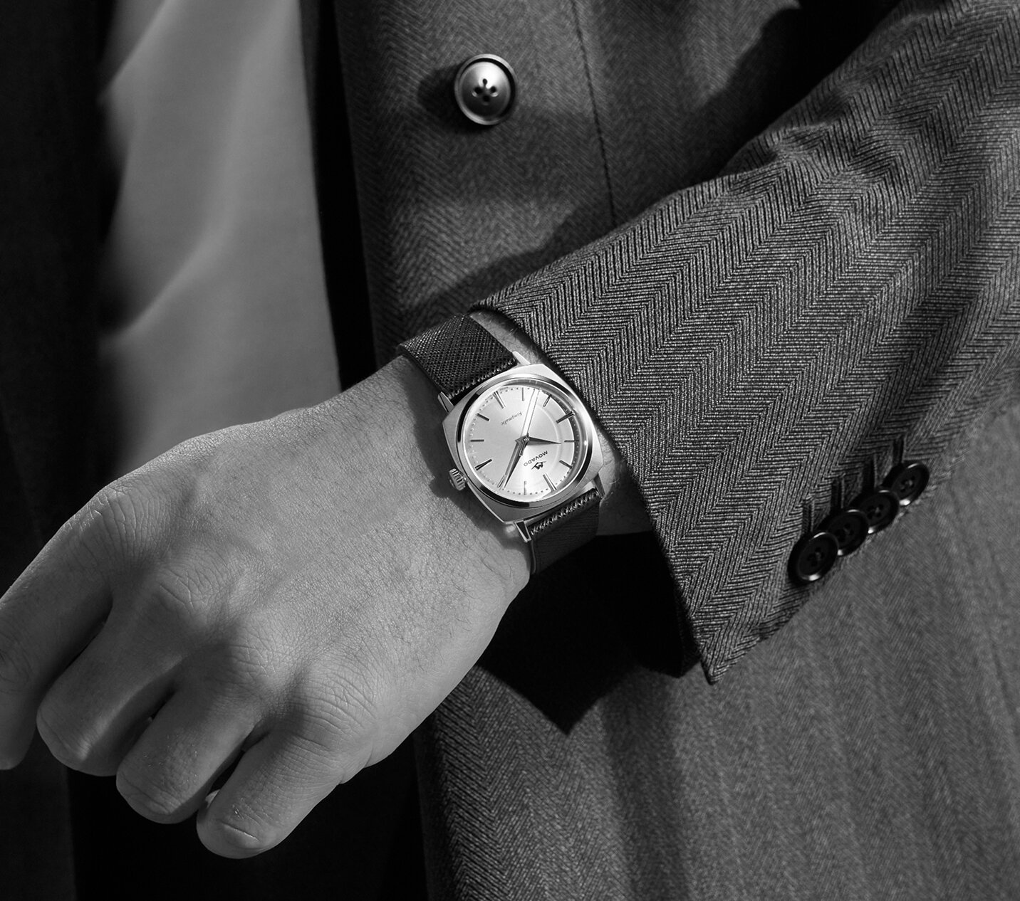 Man in a grey blazer wearing the Heritage Kingmatic watch with black leather strap and gold tone square dial.