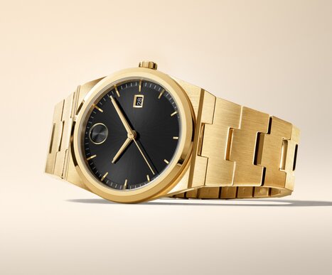 BOLD Quest watch with gold tone bracelet and black dial laying on its side.