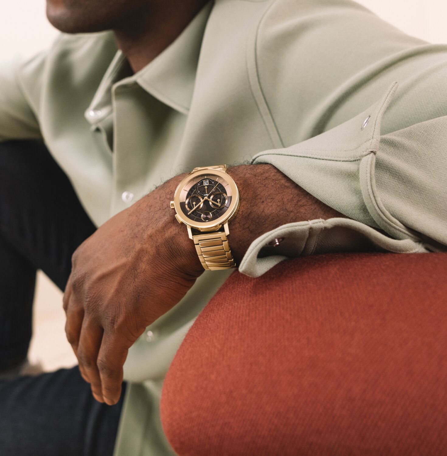 Man leaning on a sofa wearing a BOLD Evolution 2.0 watch with gold tone bracelet and brown skeleton dial.