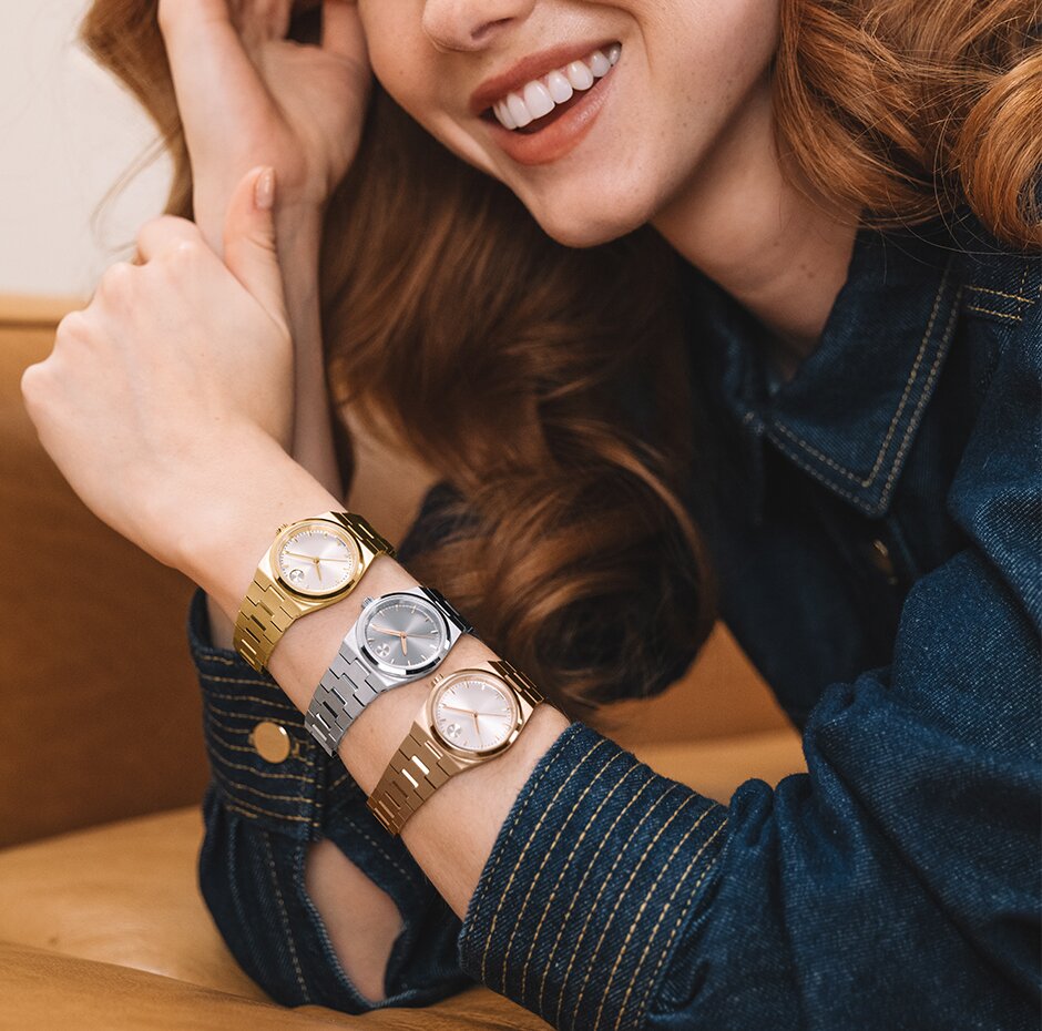 Woman in a denim shirt wearing three BOLD Quest Mini watches on her arm. Gold tone watch , silver watch and rose gold tone watch.