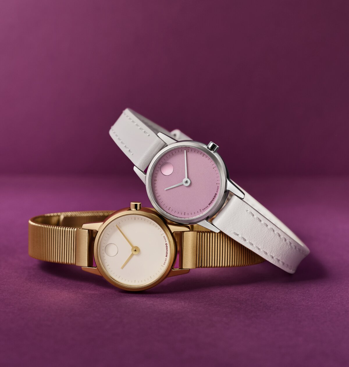 Baby Face watch with grey strap and purple dial leaning on a gold tone Baby Face watch with mesh bracelet and white dial.
