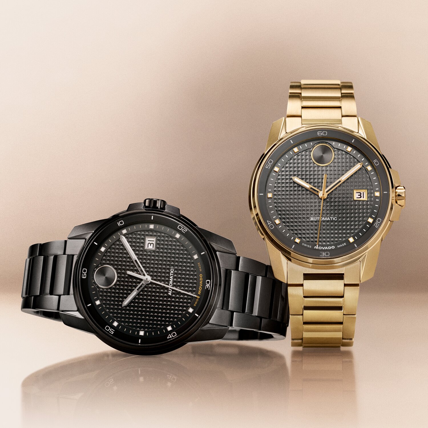 Black BOLD Verso Automatic bracelet watch laying next to a gold tone BOLD Verso Automatic bracelet watch with grey dial