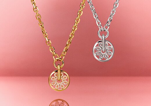 Gold tone Movado Fleur necklace featuring lab grown diamonds next to a silver Movado Fleur necklace  hanging in front of a red background 