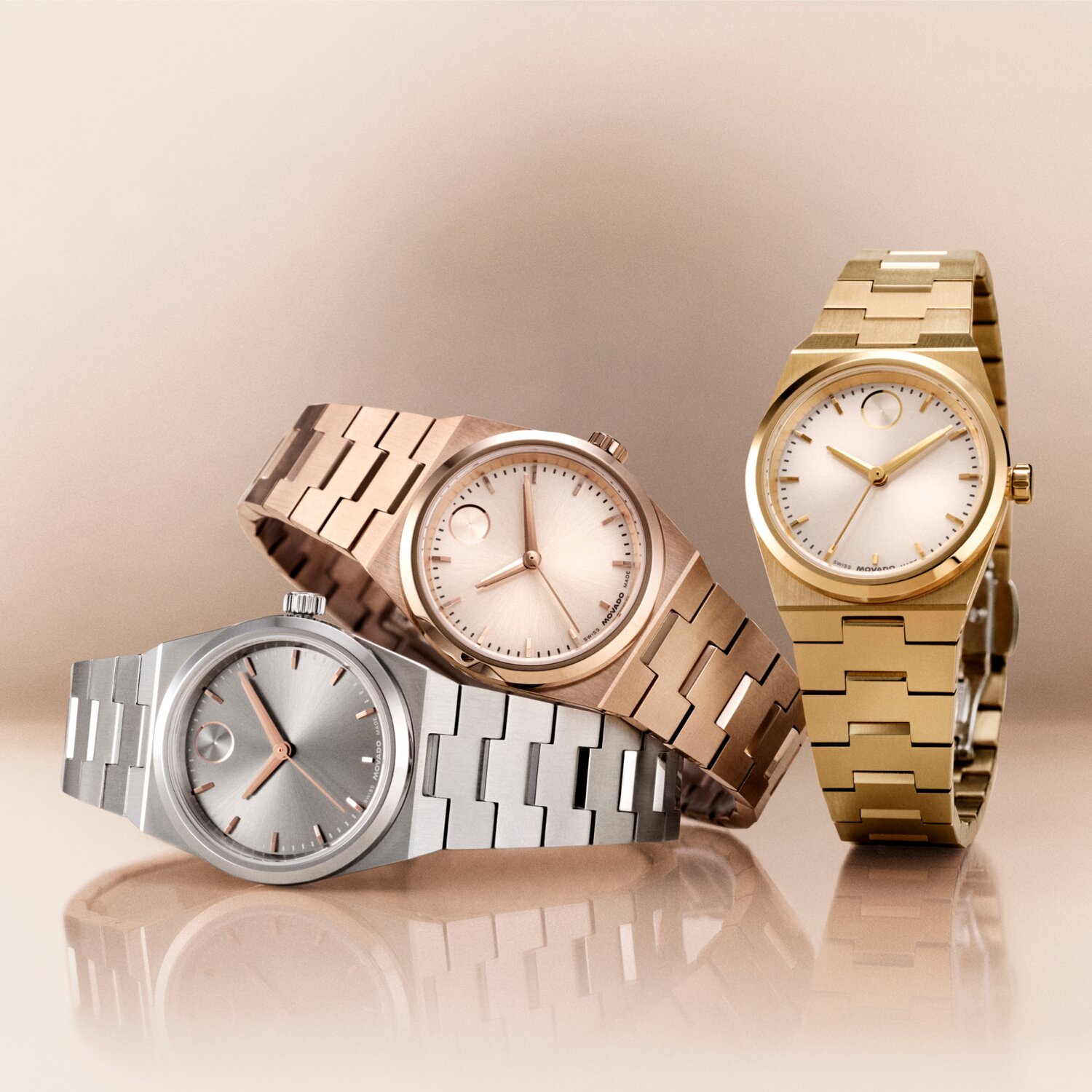 Stainless steel BOLD Quest Mini watch laying underneath a Rose gold tone BOLD Quest Mini watch with a Gold tone BOLD Quest Mini watch upright next to them.