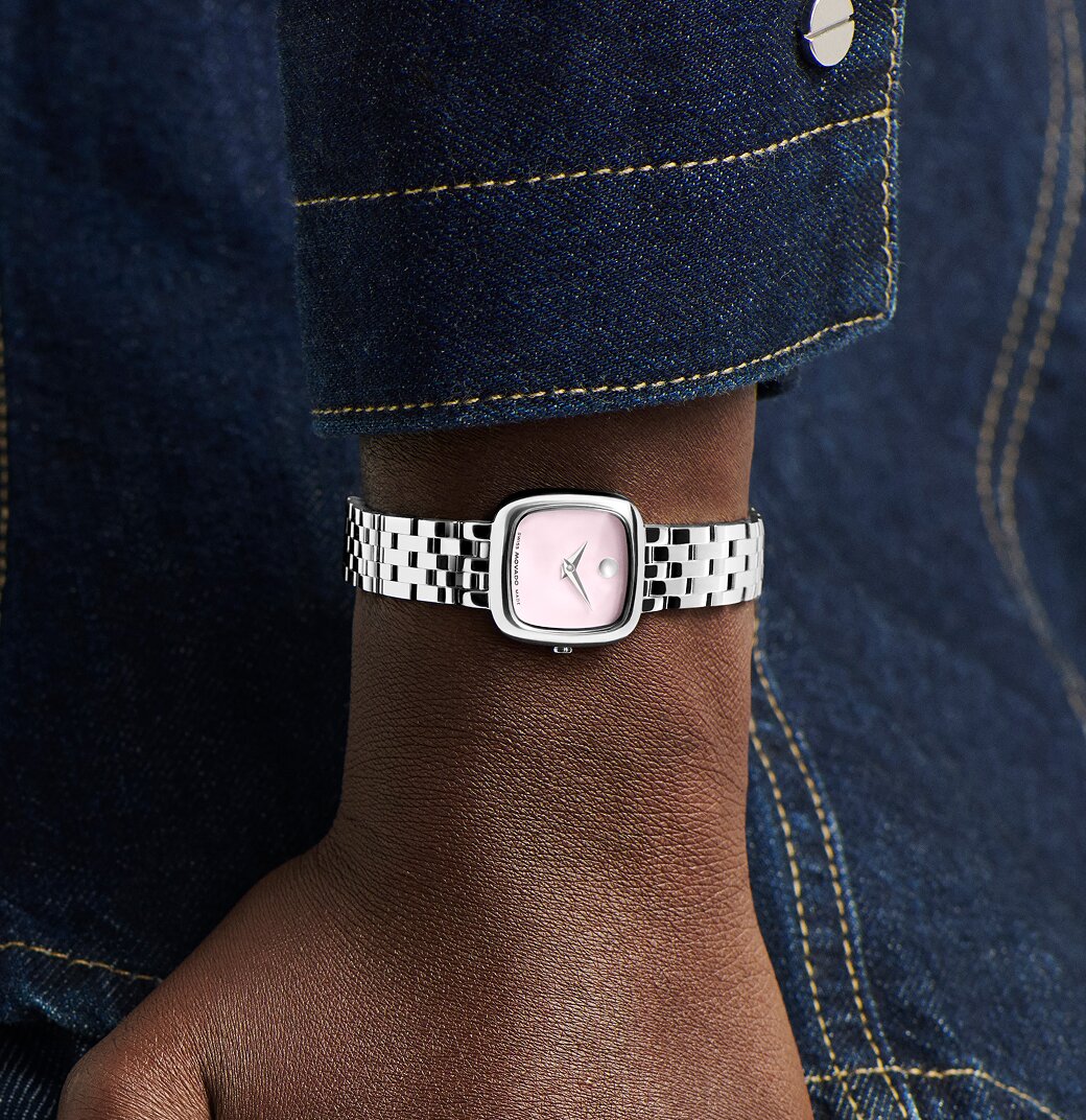 Woman in a denim jacket wearing a stainless steel Museum Classic bracelet watch with pink square dial.