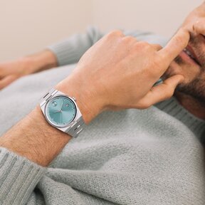 Man in a blue sweater, laying down wearing a BOLD Quest watch with stainless steel bracelet and blue dial.