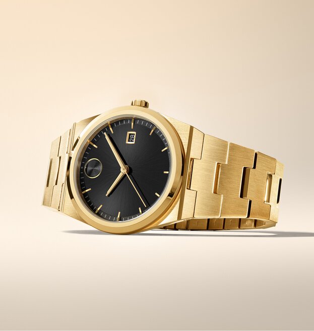 BOLD Quest watch with gold tone bracelet and black dial laying on its side.