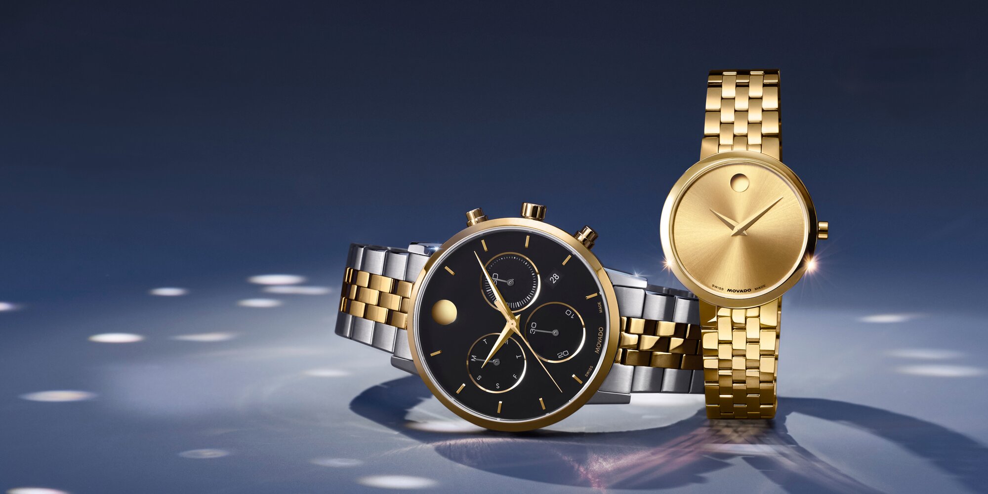 Two tone Museum Classic bracelet watch with black chronograph dial laying on its side. The women's gold tone Museum Classic bracelet watch is next to it.