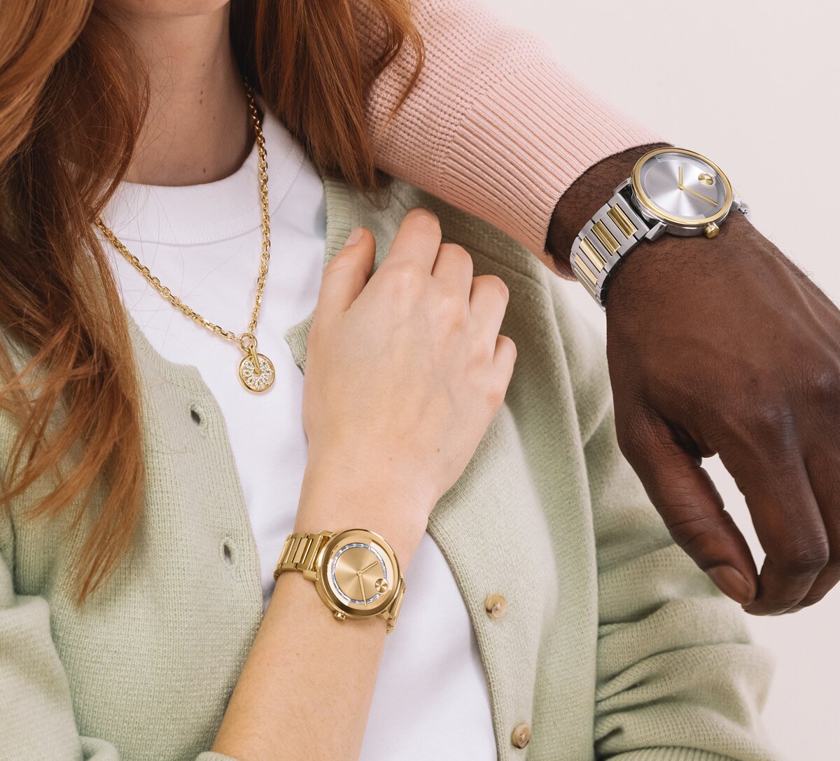 Woman in a green cardigan and white top wearing a gold tone BOLD Evolution 2.0 watch with baguette crystals and a gold tone fleur necklace with lab grown diamonds. A man in a pink sweater wearing the two tone BOLD Evolution 2.0 bracelet watch has his arm on her shoulder.