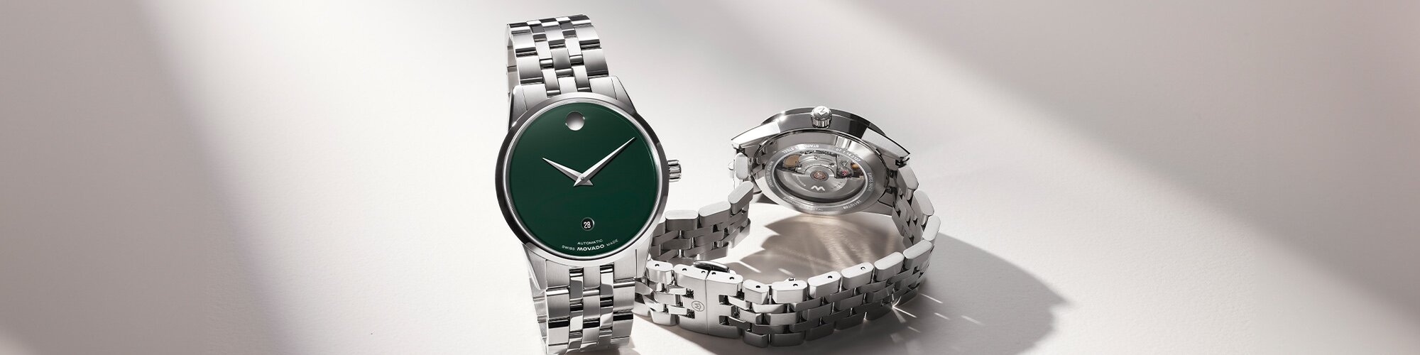 Front a silver watch with green dial and the back of the silver watch with an exposed automatic movement