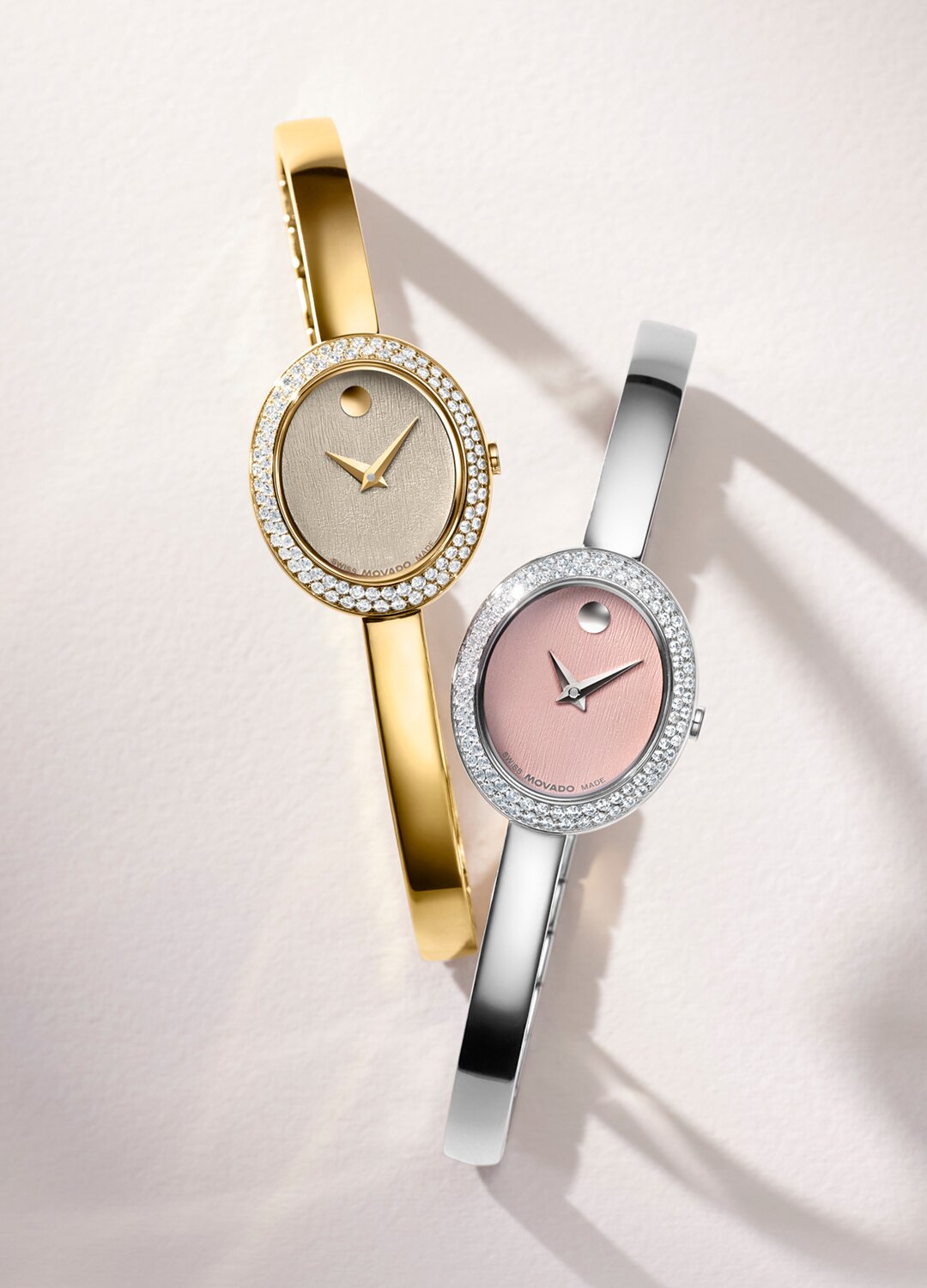 Gold tone bangle watch next to silver bangle watch with pink oval dial.