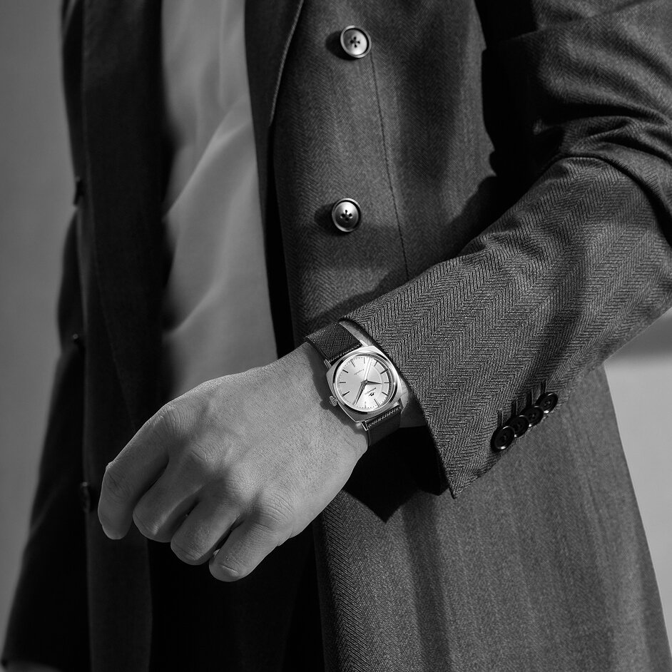 Man in a grey blazer wearing the Heritage Kingmatic watch with black leather strap and gold tone square dial.