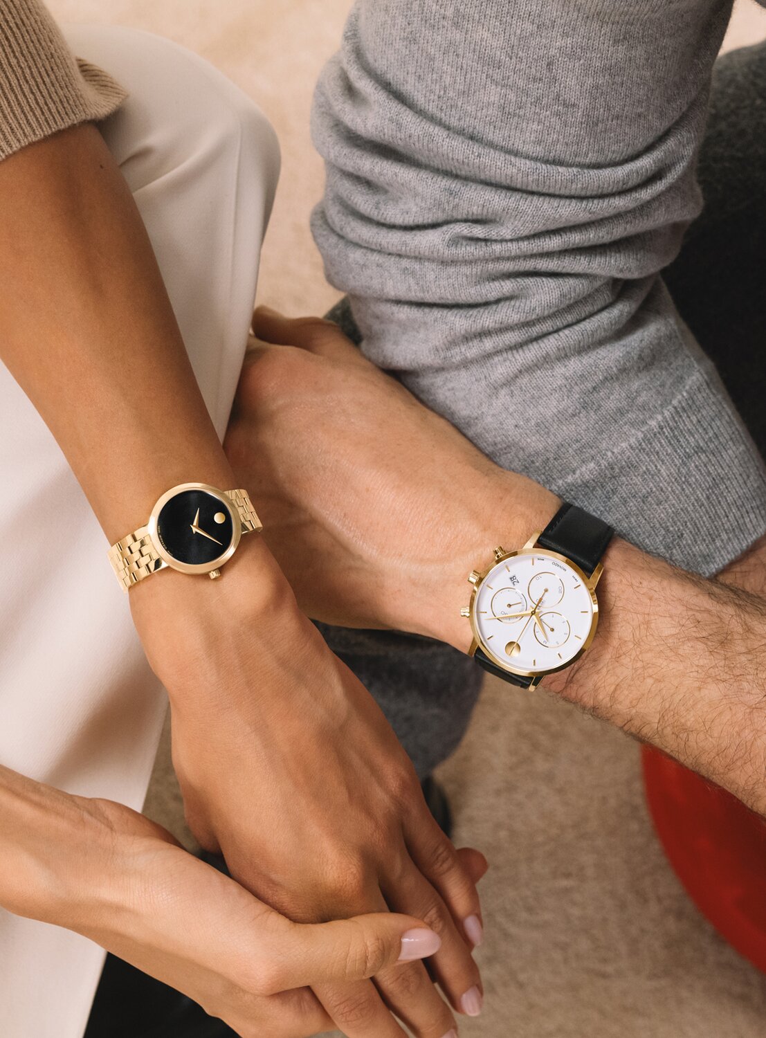 Woman wearing a gold tone Museum Classic bracelet watch with black dial sitting next to a man wearing a Museum Classic watch with a black strap and white Chronograph dial. 