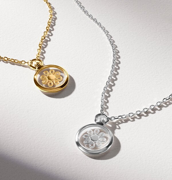 Gold tone necklace with fleur charm next to silver fleur charm necklace