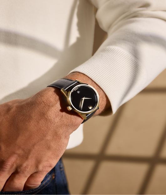 Man in a white sweater wearing the black Museum Classic watch with leather strap and gold accents.