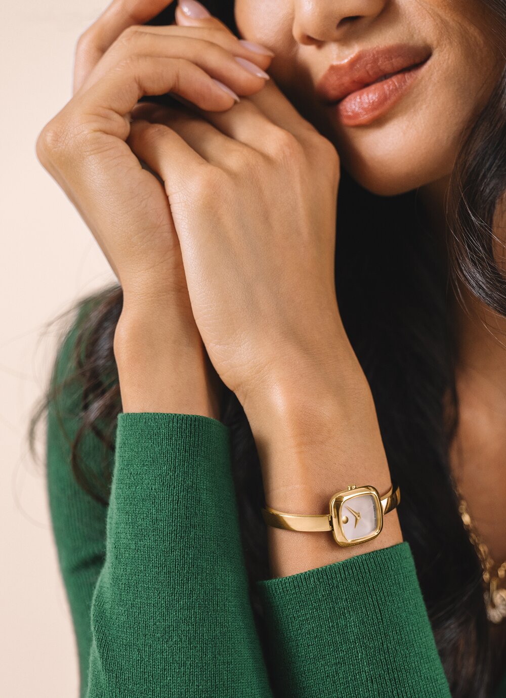 Woman in a green sweater wearing the gold tone Museum Bangle watch with white, square dia. 