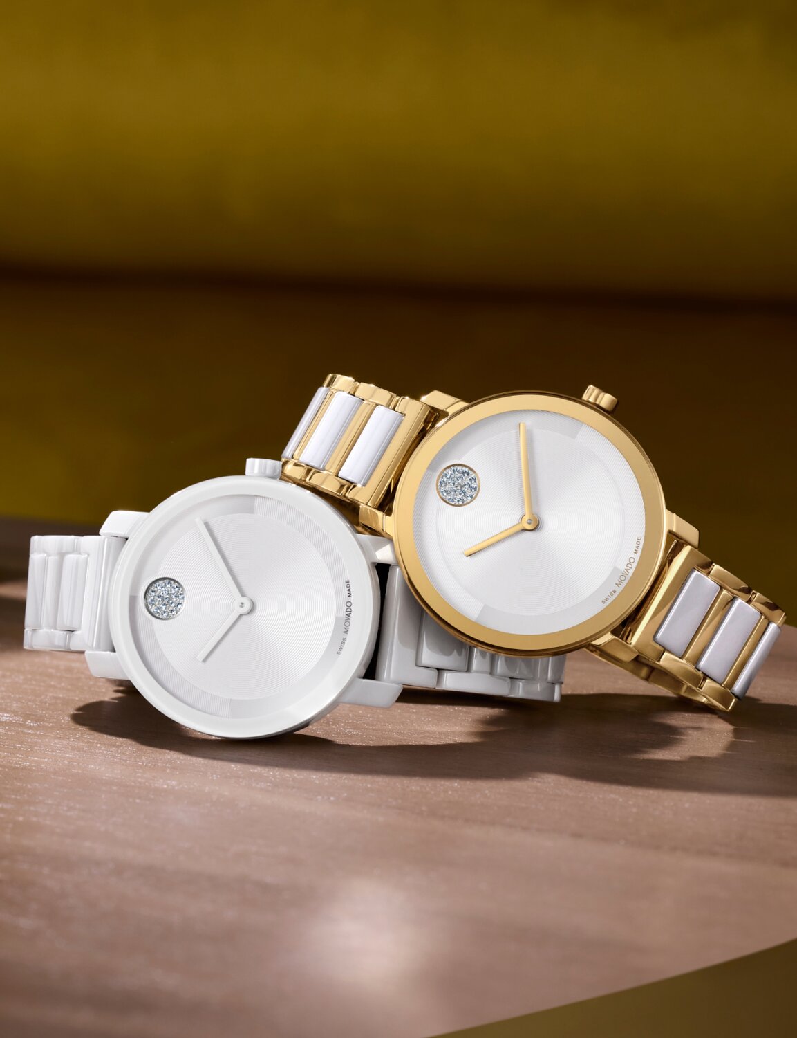 All white ceramic BOLD Evolution 2.0 watch laying underneath a gold BOLD Evolution 2.0 watch with white ceramic links on a desk