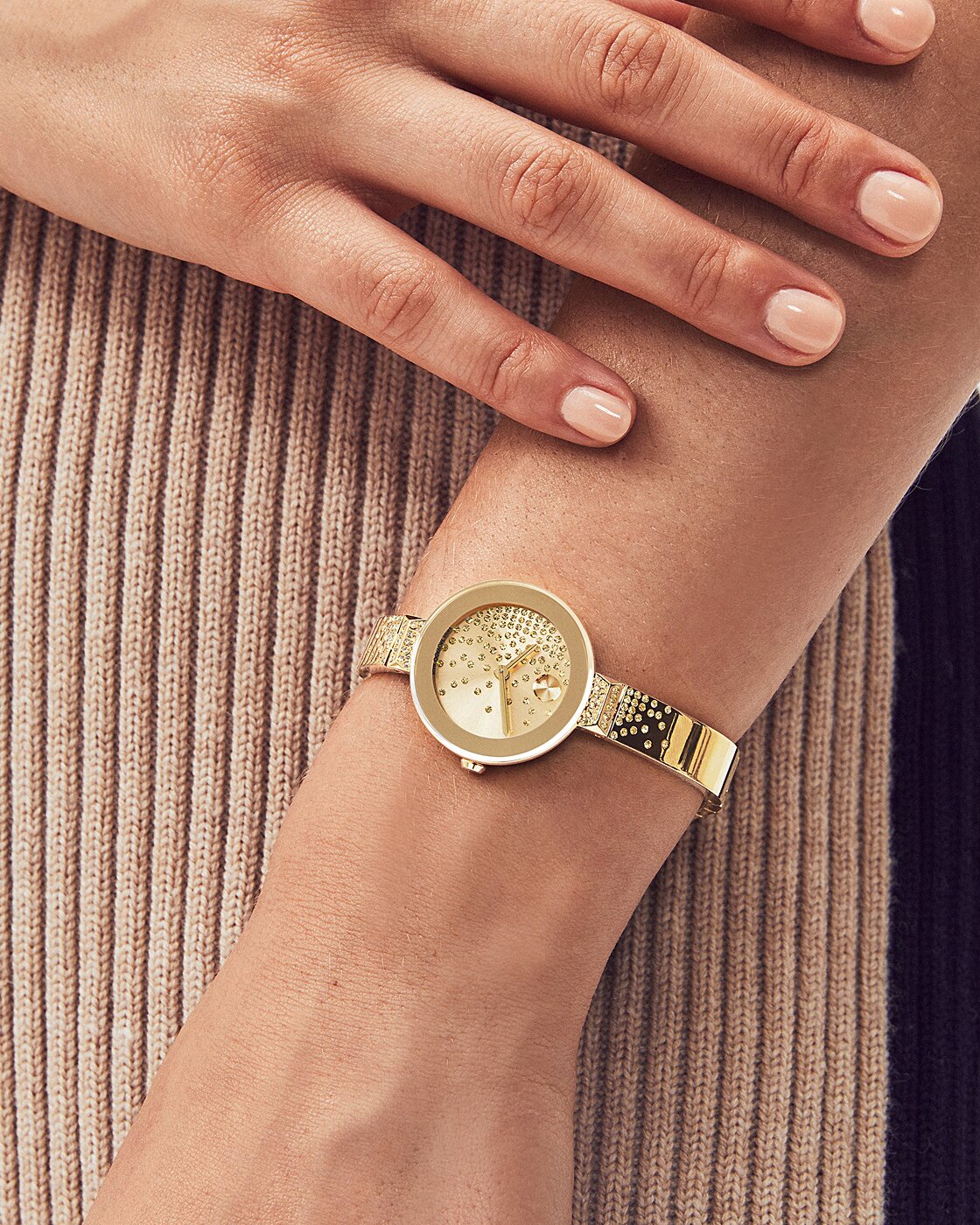 Woman in a brown sweater wearing the gold tone BOLD Bangle watch with cascading crystals on the dial and bracelet.
