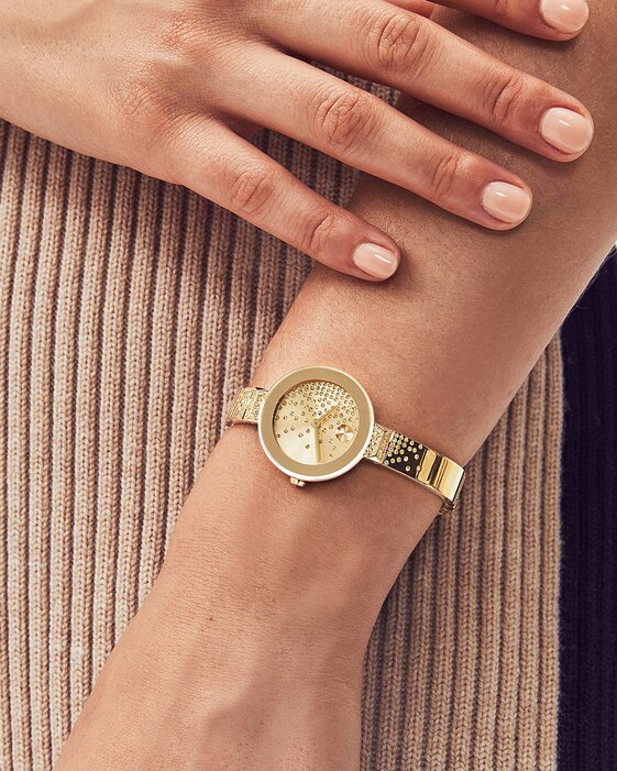 Woman in a brown sweater wearing the gold tone BOLD Bangle watch with cascading crystals on the dial and bracelet.