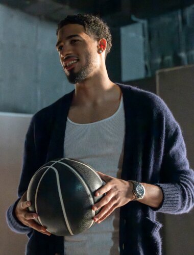 Tyrese Haliburton wearing white tank top and blue cardigan, holding a black basketball, wearing the silver SE Diver Automatic watch with blue dial.