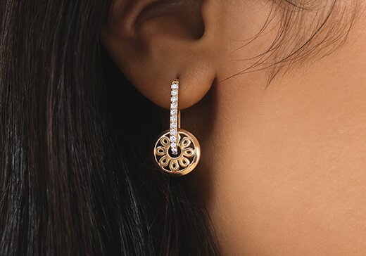 Gold tone fleur charm earring on a women's ear