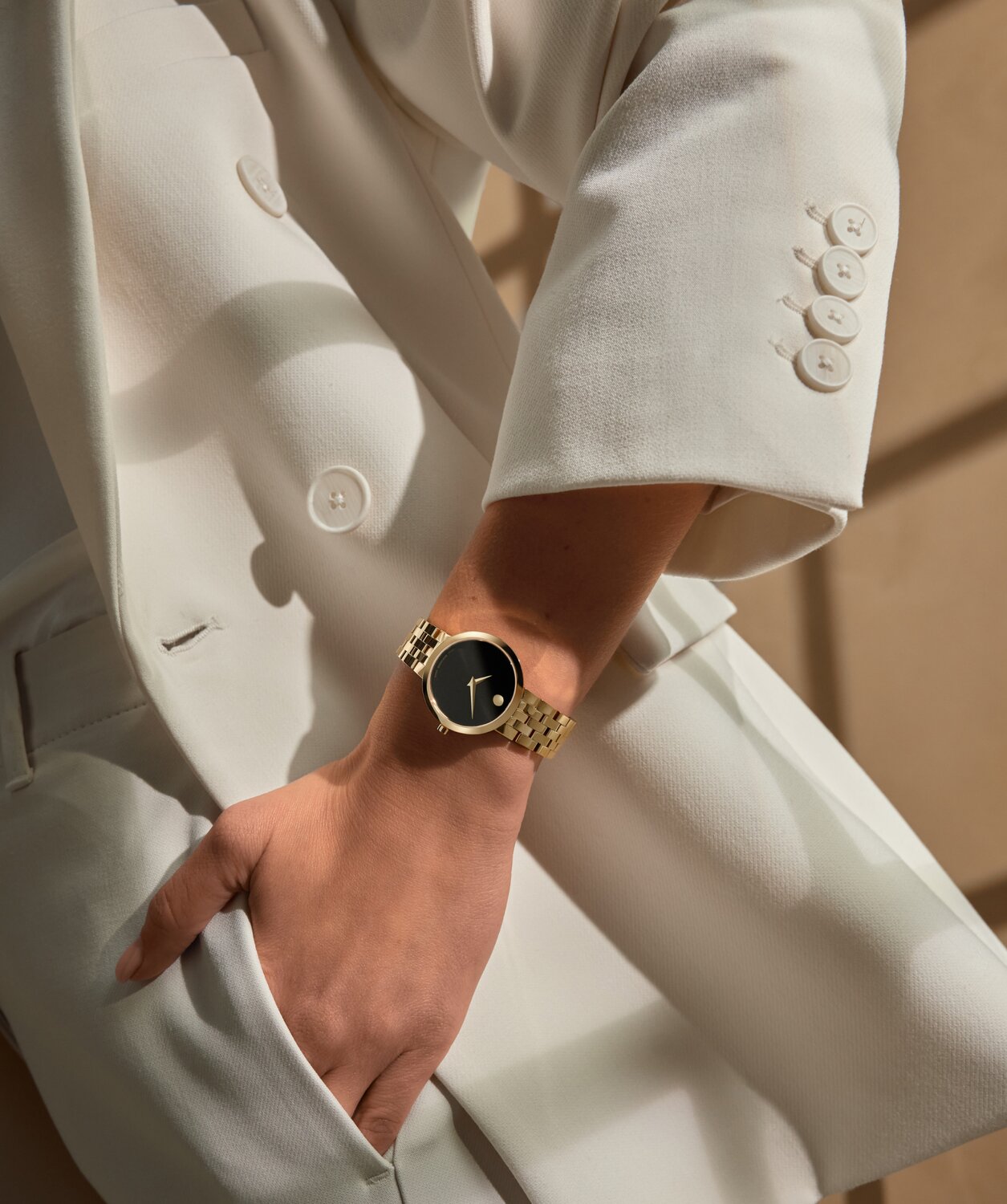 Woman in a white suite wearing the Museum Classic watch with gold tone bracelet and black dial.