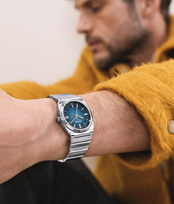Man in a yellow coat wearing the Heritage Series Ondoplan watch with silver bracelet and blue dial.
