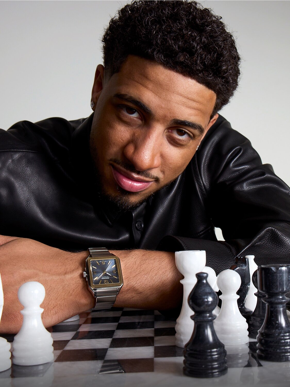 Tyrese Haliburton leaning on a black and white chess set wearing the Heritage 1917 two tone bracelet watch with square dial.