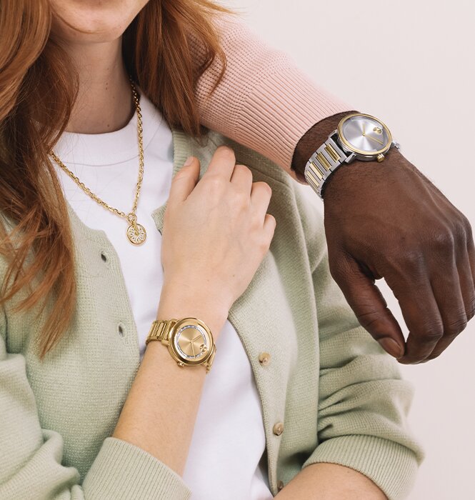 Man in a two tone Movado BOLD Evolution 2.0 watch draped over a woman wearing a gold tone fleur necklace featuring lab grown diamonds and a gold tone BOLD Evolution 2.0 watch featuring crystals.
