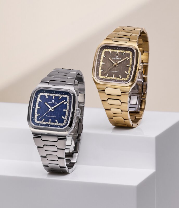 Heritage Tempo-Matic watch with stainless steel bracelet and blue TV-Shaped Case next to another Heritage Tempo-Matic watch with gold tone bracelet and brown dial.
