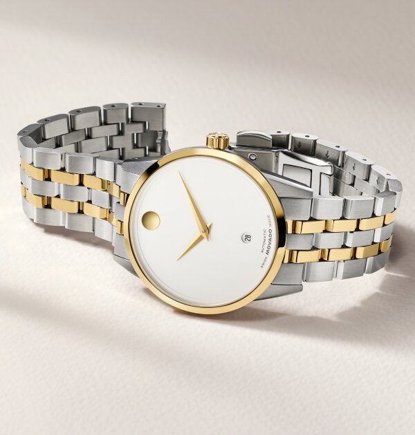Museum Classic Automatic watch with two tone bracelet and white dial with gold accents laying on its side.