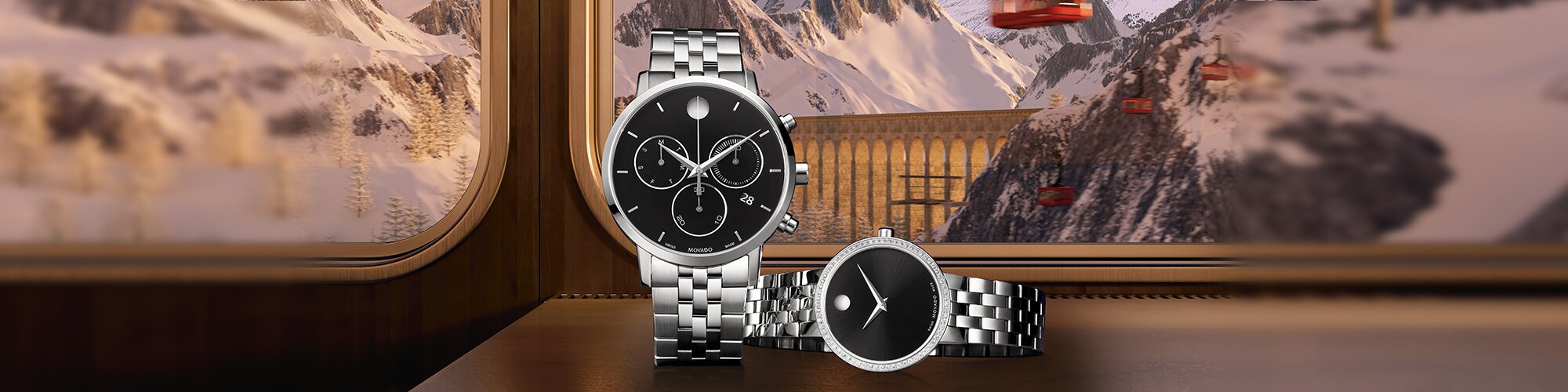 Silver watch with black chronograph dial standing next to a women's silver watch with black dial that is laying down