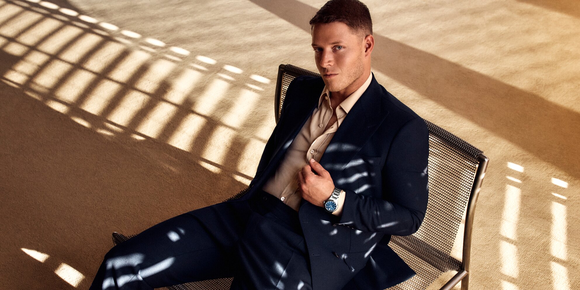 Christian McCaffrey sitting in a chair, wearing a suit and the Museum Imperial watch with silver bracelet and blue dial