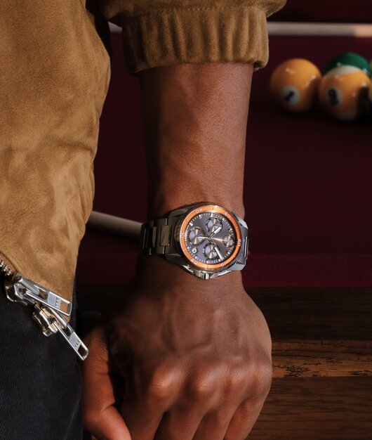 Man holding a steering wheel wearing the BOLD Verso S watch with black strap, grey dial and red hour track.
