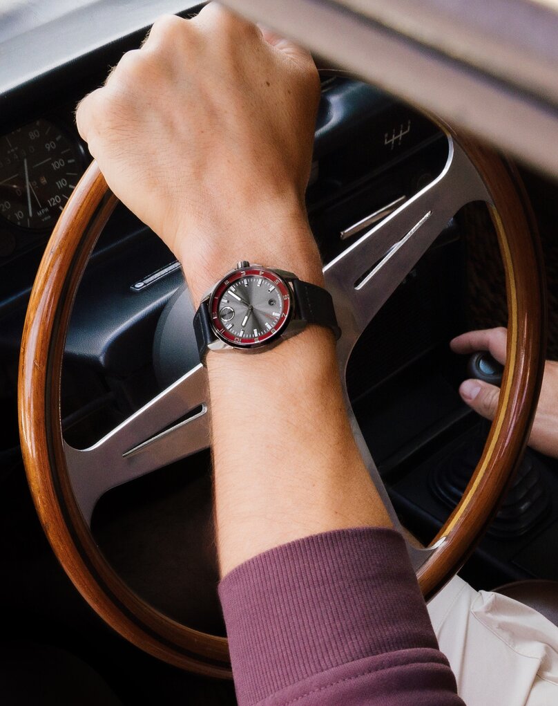 Man driving a vintage car wearing the BOLD Verso S watch with black strap, grey dial and red minute track.