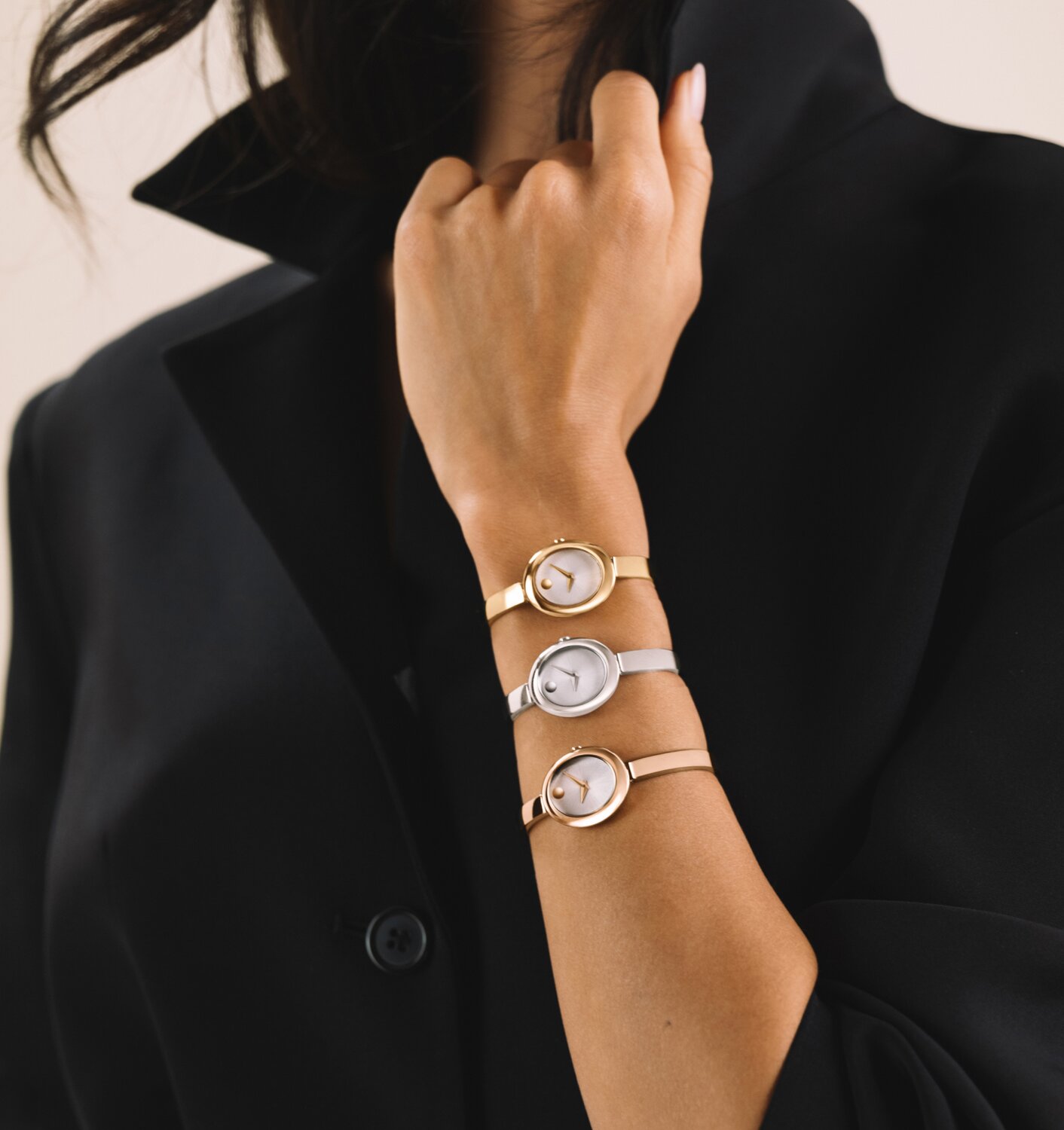 Woman in a black shirt wearing 3 Museum Bangle watches with an oval dial stacked on her wrist. Starting with the gold tone watch, followed by the silver watch and ending with the rose gold tone watch. 