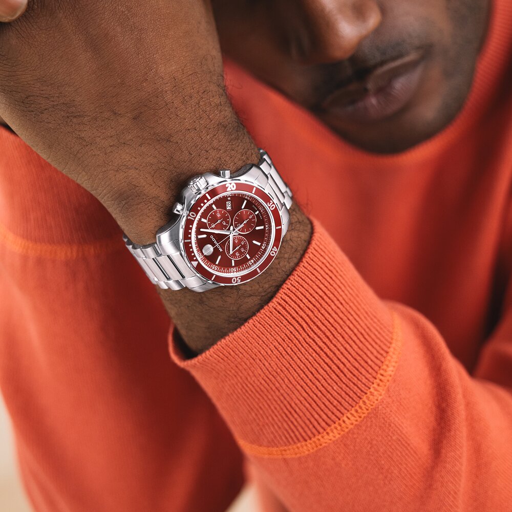 Man in an orange sweater wearing the Series 800 watch with stainless bracelet and red dial.
