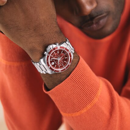 Man in an orange sweater wearing the Series 800 watch with stainless bracelet and red dial.