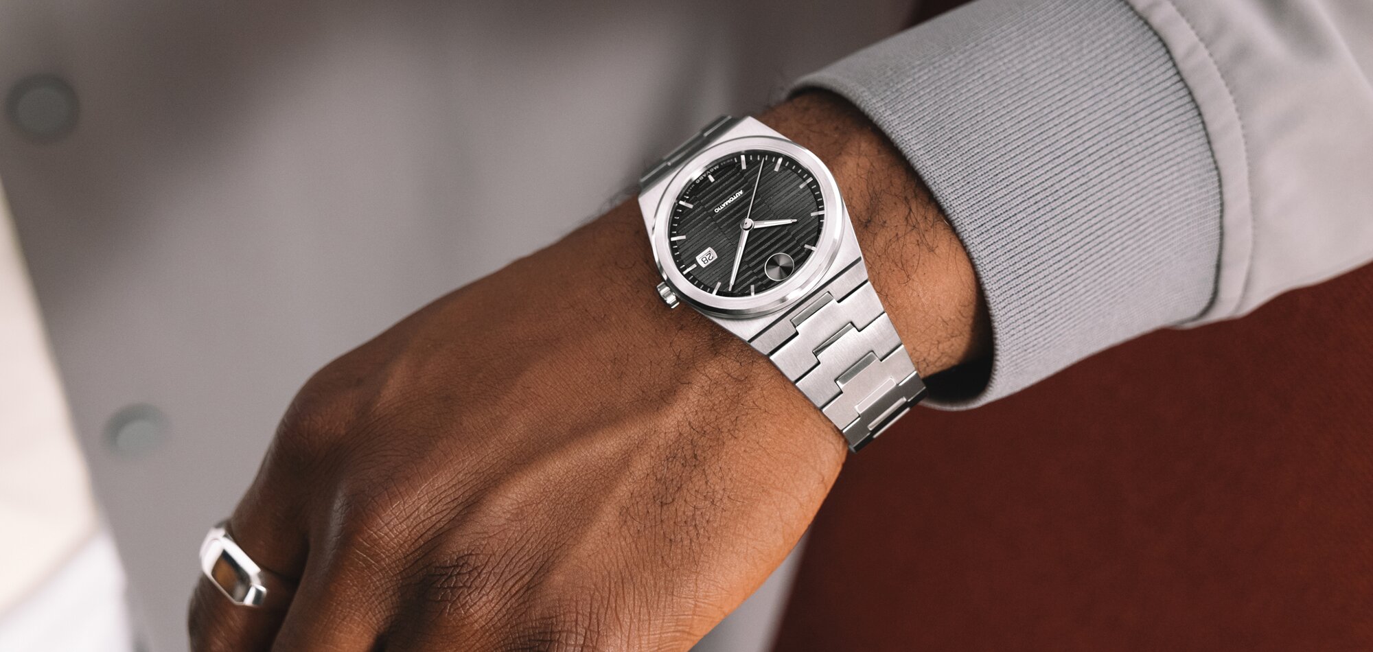 Man in a grey jacket wearing a BOLD Quest Automatic watch with stainless steel bracelet and black dial.