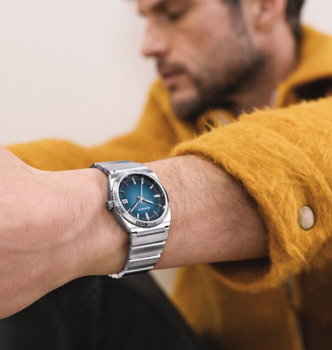 Man in a yellow coat wearing the Heritage Series Ondoplan watch with silver bracelet and blue dial.